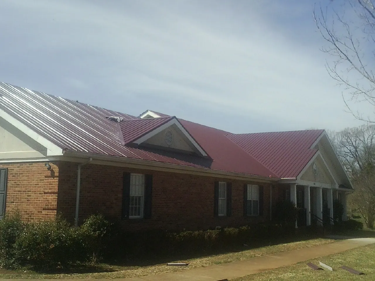 Red metal roof with gabled entries on a long brick building, from a Hail Damage Roof Repair job in Osceola