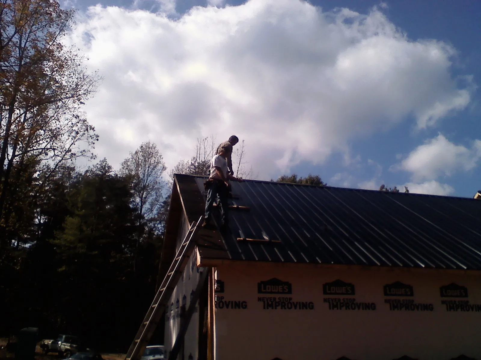 Roofer fastening dark metal panels high against a cloudy sky, from a Roof Inspection job in Osceola